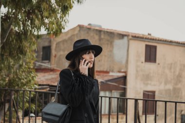 Kasaba parkında telefonla yürüyen siyahlı zarif bir kadın. . 