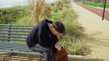 Doğada bir bankta oturan bir adam sırt çantasında bir şey arıyor. . 