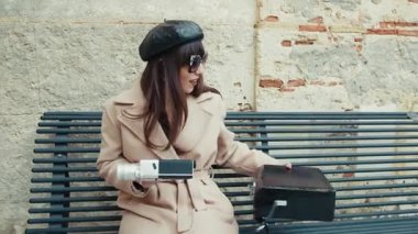 Fransız şapkalı mutlu bir kadın bankta eski bir kamerayı kaldırıyor. . 