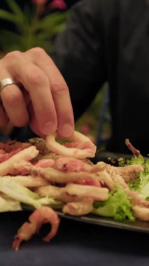 Adam yemek sırasında kızarmış mürekkep balığı halkası yemek için ellerini kullanıyor. .