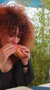 Sahildeki restoranda öğle yemeği için hamburger yiyen bir kadın. . 