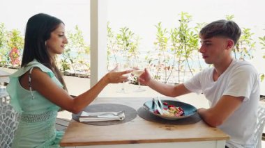 İki erkek ve bir kız, deniz kenarındaki bir restoranda lüks bir şaraptan içerler..