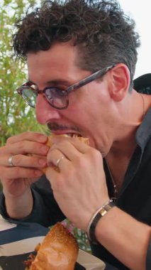 Adam sahildeki restoranda öğle yemeğinde hamburgerin tadını çıkarıyor. . 