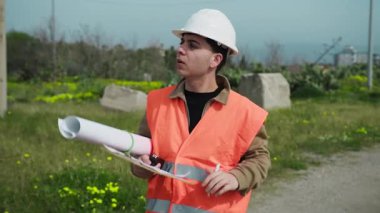 Mimar inşaat sahasında yürürken not alıyor ve etrafa bakıyor..