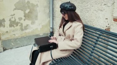 Bankta oturan bir kadın eski model kamerayla çantayı açıyor. . 