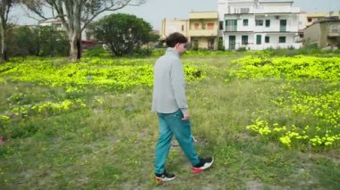 Doğada yürüyen ve otlardan sarı bir çiçek toplayan bir adam. . 