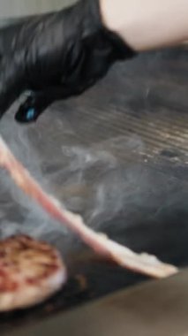 Şef et pişirirken ızgaraya domuz pastırması ekliyor. . 