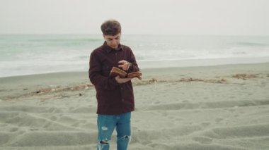 Okyanusun kenarında dua eden bir adam İncil 'in sayfalarını çeviriyor. . 