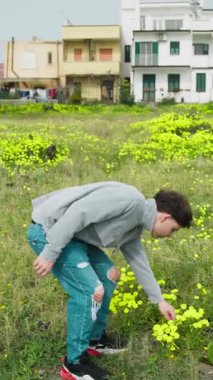 Doğada yürüyen ve otlardan sarı bir çiçek toplayan bir adam. . 