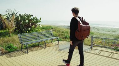 Üniversite öğrencisi okyanusun kenarındaki bir bankta dinleniyor. . 