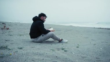 Üzgün adam, kışın kumların üzerinde oturan bir kitap okumaya başlar..