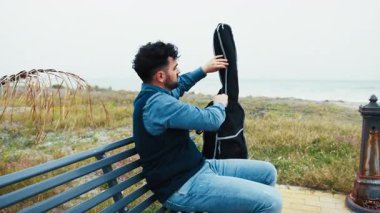 Adam Gitarını Deniz kenarında çalmak için çantayı açar.. 