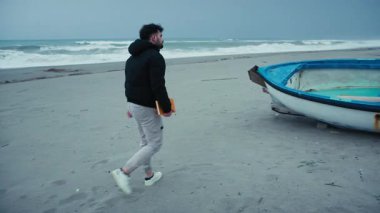 Adam bulutlu bir günde denize varır ve okumak için bir teknede oturur.. 