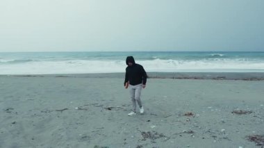 Elinde bir kitap tutan adam kışın deniz kenarında tek başına yürüyor..