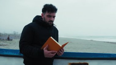 Adam kışın deniz kenarında dinlenirken dikkatle kitap okur.. 