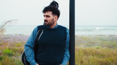 Gitarist, Deniz kenarındaki bir kutba yaslanan birini bekliyor.. 