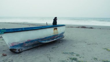  Kışın denizdeki adam kitap okumak için bir tekneye yaslanır.. 
