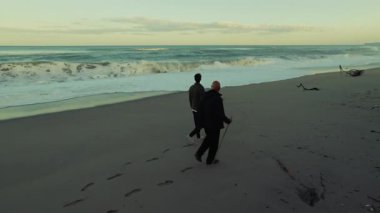 İki Adam Fırtınalı Okyanus Dalgaları 'nın Sabah Kumsalda Düştüğünü İzler.