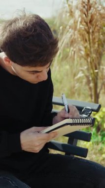 Üniversite öğrencisi, deniz kenarındaki bir bankta notlar yazıyor ve okuyor. . 