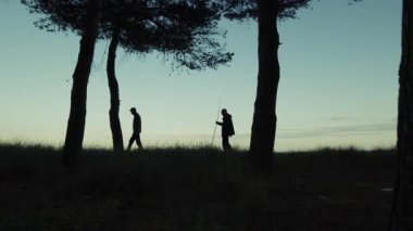 Sabahın köründe denize yakın ağaçların arasında yürüyen iki kişinin silueti..