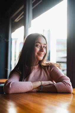 Portrait of girl looking at camera. She is sitting at a table in a bar.