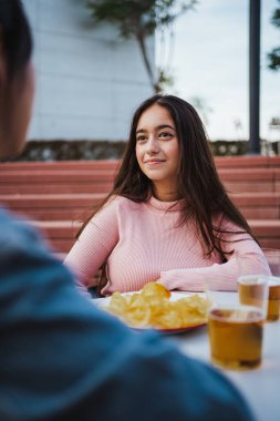 Portrait of girl having a conversation with her friend at a bar terrace while having a beer