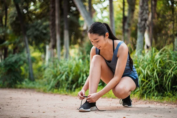 stock image Shot of smiling asian sport girl tying her shoe laces in the park