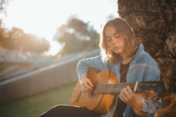 Foto Retroiluminada Uma Jovem Mulher Concentrada Enquanto Tocava Guitarra Parque — Fotografia de Stock