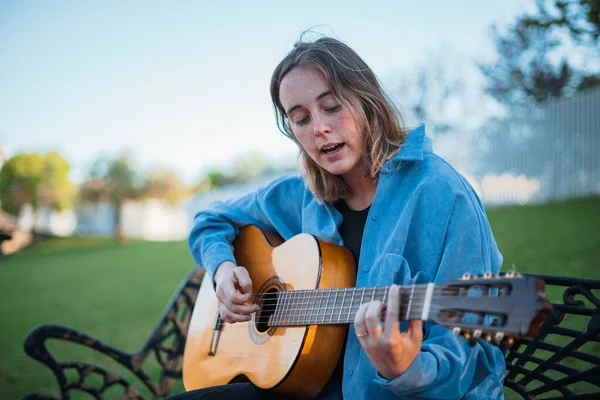 Молода Жінка Співає Грає Гітарі Одночасно Вона Сидить Лавці Парку — стокове фото