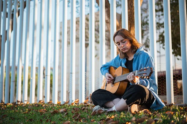 가난젊은 여자가 울타리에 기대어 기타를 연주하고 있었다 공원에 있어요 — 스톡 사진