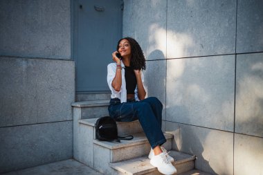 Neşeli Afrikalı bir genç merdivende otururken cep telefonuyla konuşuyor.