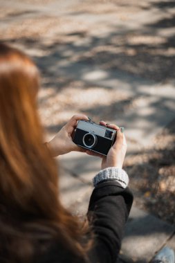 Genç bir kadın bankta eski bir analog kamera kullanarak selfie çekiyor..