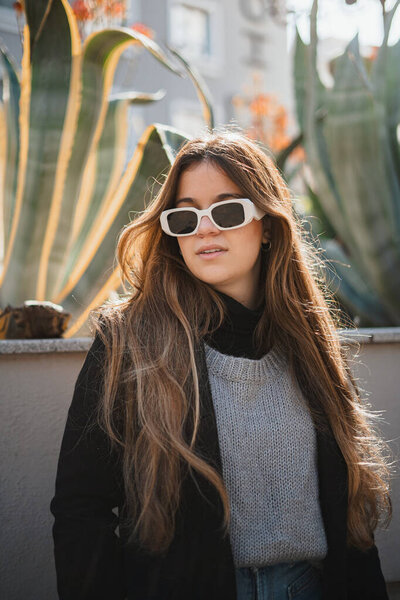 Portrait of a teenage girl wearing white sunglasses during a sunny day. There are plants at the background.