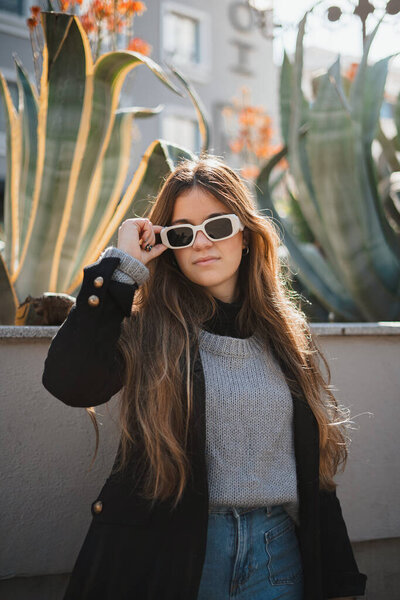 Portrait of young woman posing and touching her sunglasses during a sunny day