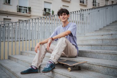 Kaykay çalışmasından dinlenen genç adam. Beton merdivenlerde oturuyor.