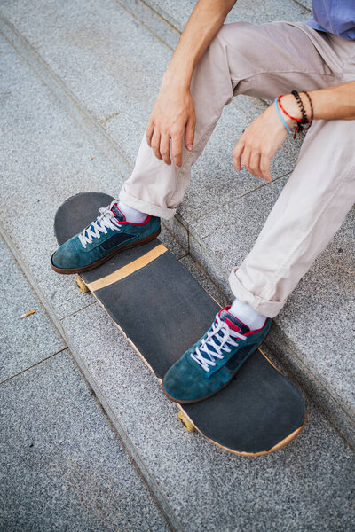 Cut out shot of legs of a young man on a skateboard while he is sitting on stairs