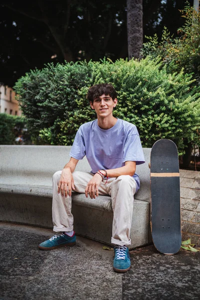 Portrait of smiling skater young man looking at camera. He is sitting on a concrete bench.