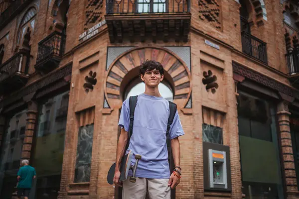 Portrét Usměvavého Bruslaře Mladého Muže Držícího Skateboard Nesoucího Batoh Městě — Stock fotografie