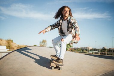 Kaykayını beton bir rampada sürmeye odaklanmış genç bir adam.