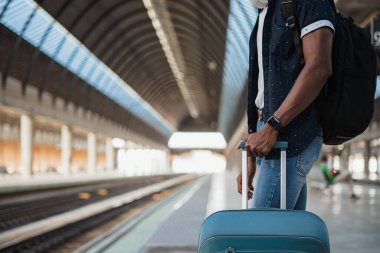 Treni beklerken çekilen siyah adam. Elinde mavi bir valiz var..