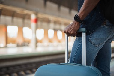 Bir tren istasyonunda tren beklerken elinde bavul tutan Afrikalı adamın yakın plan fotoğrafı.