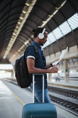 Afrikalı gezgin, tren istasyonunda beklerken şehirde bir yer bulmak için harita okuyor.