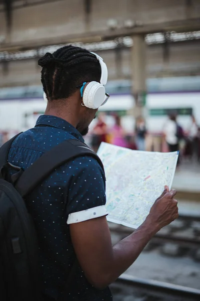 Perspective shot of african man listening to music and looking at a map in a train station