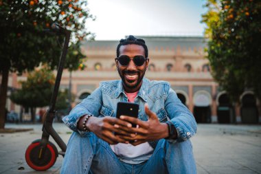 Mutlu genç adam dışarıda arkadaşıyla görüntülü konuşma yapmak için akıllı telefonu kullanıyor.