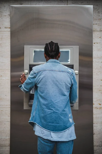 Young man using an ATM to withdrawal money. He is traveling abroad and needs some cash.