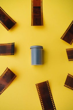 Sarı arkaplanda negatiflerle çevrili film kutusunun yüksek açılı görüntüsü