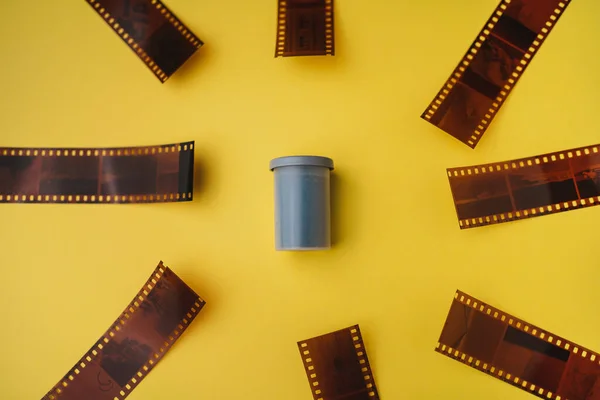 High angle shot of film roll canister surrounded by negatives on yellow background