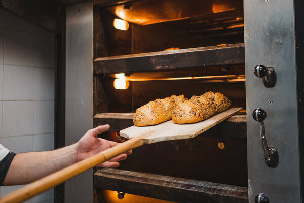 Anonymous man taking seed bread out with shovel from oven in bakery