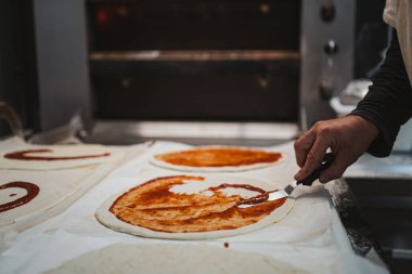 Fırıncı fırına koymadan önce pizza hamuruna domates sosu döker.