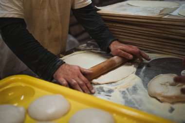 Fırıncı adam fırının mutfağında pizza hamurunu oklavayla düzleştiriyor.